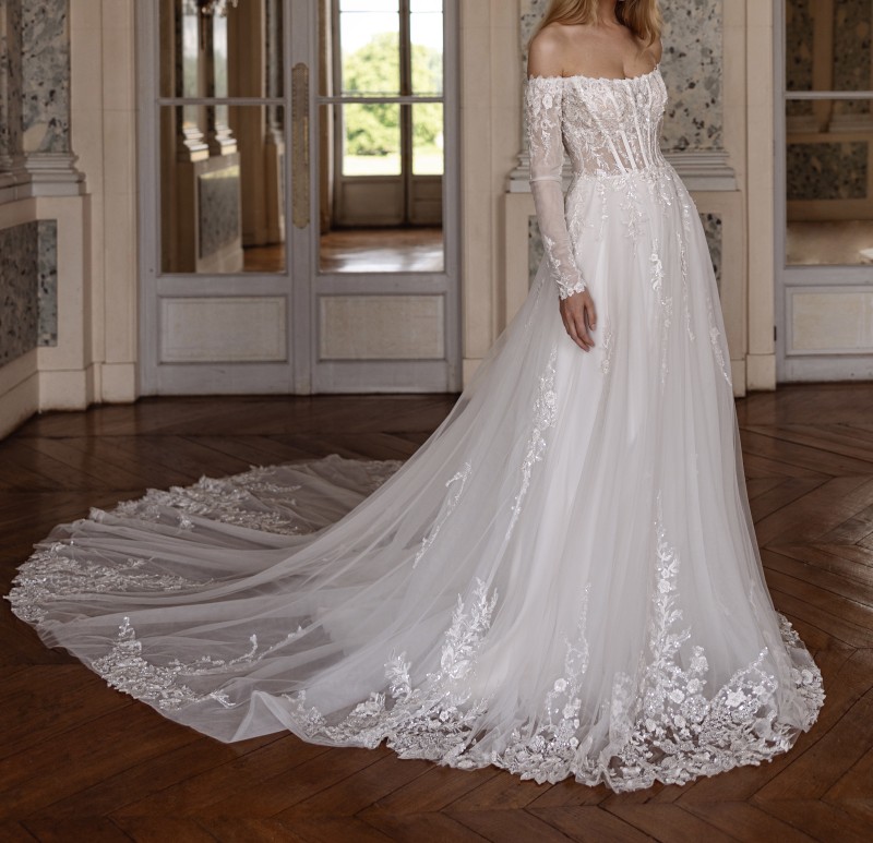 Découvrez notre robe de mariée princesse Arisa de la collection 2025 de la créatrice Anna Sposa, col bateau, manches longues et une majestueuse traine à Marseille